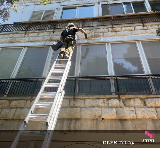 אדם על סולם עובד על קיר חיצוני של בניין
